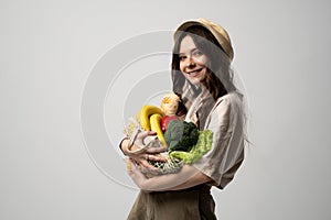 Zero waste concept. Brunette woman in a beige t-shirt and a hat with a mesh bag full of fresh vegetables and fruits