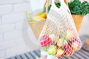 Zero waste concept with copy space. Woman holding straw basket and reusable mesh shopping bag withapples, vegetables, white brick