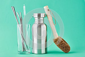 Zero waste concept. Eco friendly reusable items aluminun bottle and metal tubes in glass on a green background