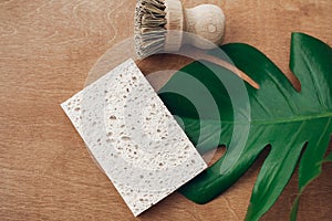 Zero waste concept, flat lay. Reusable natural cellulose sponge and eco wooden brush on wooden background with green monstera leaf photo