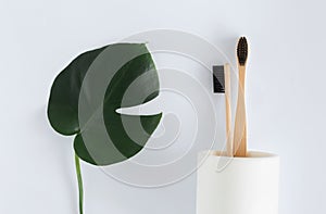 Zero waste concept. Natural eco bamboo toothbrush in stand with monstera leaves white background top view Copy space