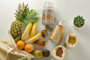 Zero waste and plastic free concept. Grocery shopping eco bag with fruits and cereals in glass jars, white background. Flat lay,