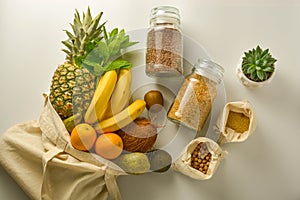 Zero waste and plastic free concept. Grocery shopping eco bag with fruits and cereals in glass jars, white background. Flat lay,