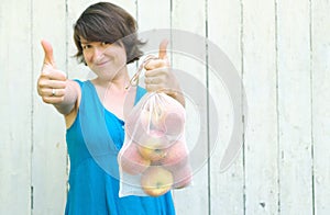 Zero waste shopping concept. No single use plastic. Woman holding reusable recycled mesh produce bag with apples and showing sign