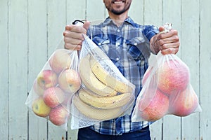 Zero waste shopping concept. Smiling man holding reusable eco bags with fresh fruits. Ban single use plastic