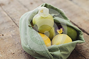 Zero waste shopping. Fresh apples, avocado, lemons in eco cotton bag with flower on rustic wood