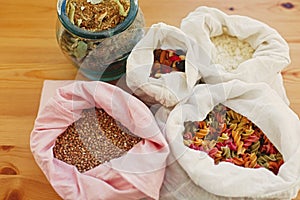 Zero waste shopping. Groceries in reusable textile bags on wooden table. Cereals,pasta, flour, grains in bags, tea in glass jar.
