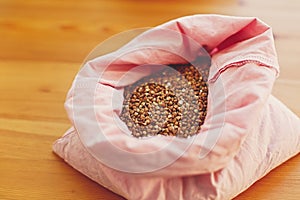 Zero waste shopping. Organic buckwheat grain in reusable bag close up. Groceries in reusable textile bags on wooden table. Plastic