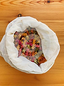 Zero waste shopping. Organic colorful pasta in reusable bag close up. Groceries in reusable textile bags on wooden table. Plastic