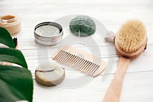 Zero waste solid shampoo bar, bamboo toothbrushes, wooden brush, natural deodorant and konjaku sponge on white wood with green mo