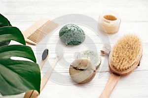 Zero waste solid shampoo bar, bamboo toothbrushes, wooden brush, natural deodorant and konjaku sponge on white wood with green mo