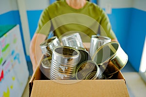 Zero waste sustainability concept. Close up selective focus of man holding brown carton box of metal tin cans to be recycled.