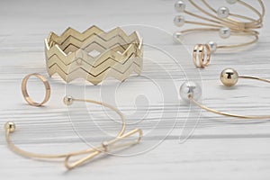 Zigzag shape golden bracelet between golden girl accessories on wooden table