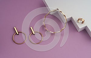 Zigzag shape golden bracelet and modern earrings pair on white and pink geometric background with copy space