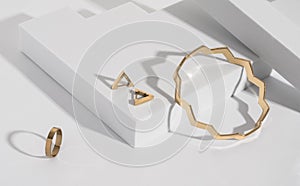 Zigzag shape golden bracelet and modern earrings and ring on geometric white background