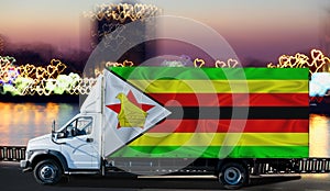 Zimbabwe flag on the side of a white van against the backdrop of a blurred city and river. Logistics concept