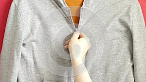 Zipper on the clothes is unfastened by female hands, under it is an orange T-shirt
