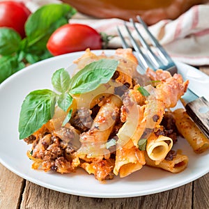Ziti bolognese on a white plate, pasta casserole with minced meat, tomato sauce and cheese, square