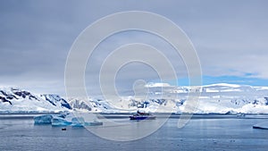 Zodiac and expedition cruise ship among icebergs in a bay in Antarctica