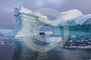 A zodiac full of tourist viewed through an arch in a large iceberg, Antarctica