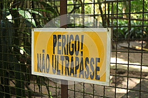 Zoo yellow warning sign in portuguese: `Perigo, nÃ£o ultrapasse!`