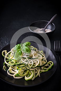 Zoodles, zucchini noodles with parmesan and basil on a black plate on black background