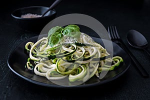 Zoodles, zucchini noodles with parmesan and basil on a black plate on black background