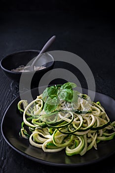 Zoodles, zucchini noodles with parmesan and basil on a black plate on black background