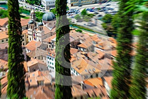 Zoom blurred top view of the old town in Kotor focused on a church through green trees. Montenegro