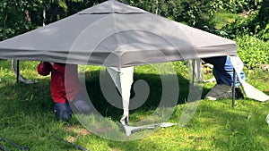 Zoom in father and son fix tent cloth roof on garden arbour