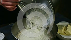 Zoom in at female hands by whisk sprinkle out flour into liquid dough in metal bowl