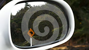 Zoom in on a kiwi road sign reflected in a car mirror