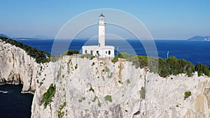 Zoom out drone shot of white lighthouse on a cliff.