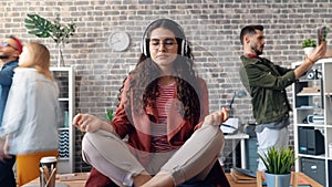 Zoom out of lady listening to music relaxing in office on table in lotus pose