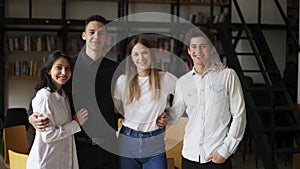 Zoom out portrait of four multiethnic young people standing together in group looking at camera posing at library or in