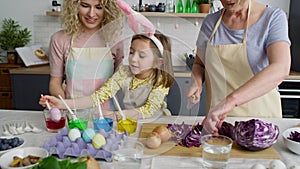 Zoom out of three generations of women preparation Easter eggs.