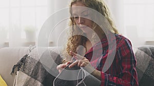 Zoom out of young woman sitting on couch and knitting in home