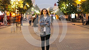 Zoom in time-lapse of stylish young lady tired of usual haste standing in the street among whizzing people and looking