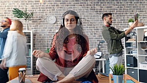 Zoom in time-lapse of woman listening to music in lotus pose on office desk