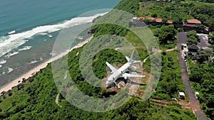 Zoom to airplane on edge of cliff in green tropical paradise near ocean. Abandoned aircraft in Bali island with