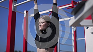 Zoom in to motivated woman trying to do pullups in slow motion in sunshine. Side angle view portrait of self confident