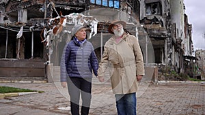 Zoom in to sad senior man and woman looking around standing in ruined Ukrainian city taking hands of each other in slow