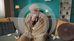 Zoom in video of an eldery, retired man, senior citizen sitting on a couch, sofa wrapped in blanket, coughing as if he