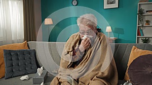 Zoom in video of an eldery, retired man, senior citizen sitting on a couch, sofa wrapped in blanket, measuring his