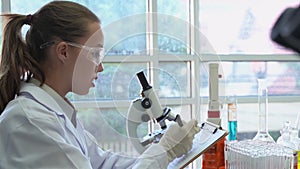 Zoom in video shot of Young female scientists took a test tube to analyze and use a pen to record the results on paper.