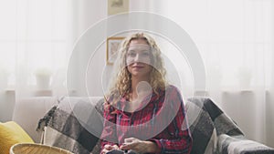 Zoom in of woman sitting on sofa, knitting in home and looking in camera