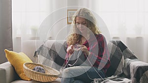 Zoom in of young woman sitting on couch and knitting in home