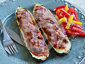 Zucchini boats, filled zucchinis on a plate served with bell peppers and parmesan cheese