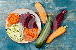 Zucchini, carrot, sweet potato and beetroot noodles on a plate. Top view, overhead. Blue rustic background.