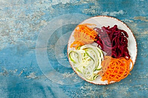 Zucchini, carrot, sweet potato and beetroot noodles on a plate. Top view, overhead. Blue rustic background.